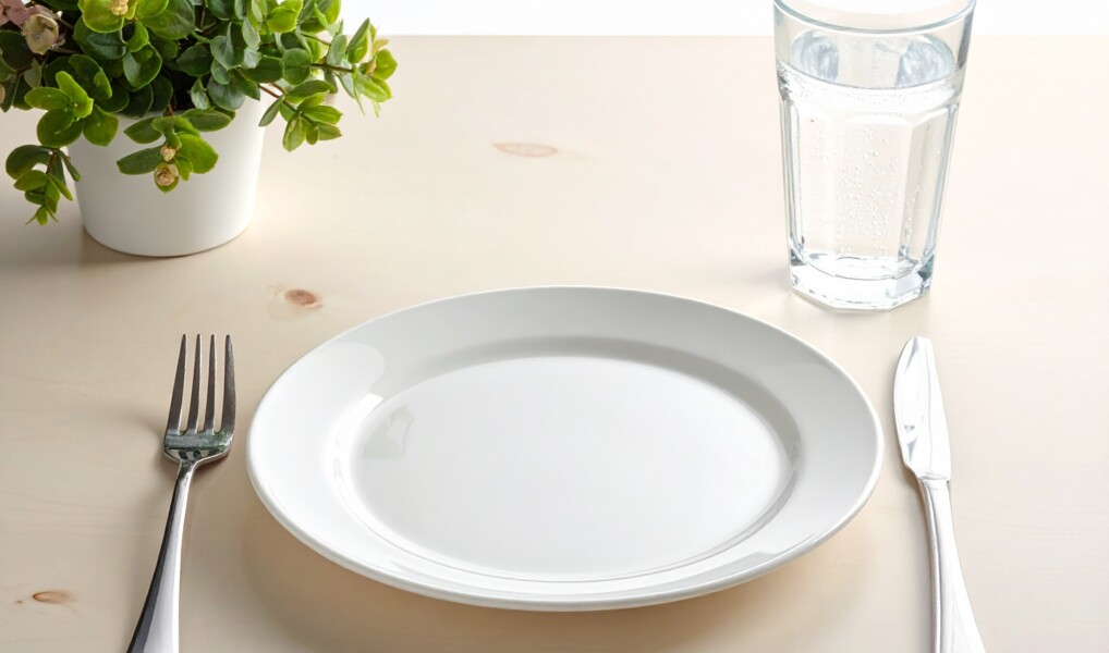 En hvid tallerken på et bord med kniv, gaffel og et glas vand