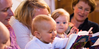 Mødre med deres babyer bladrer i en sangbog ved babysalmesang i en kirke