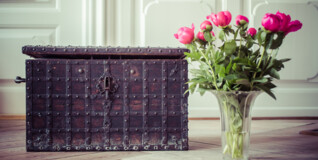 En gammel pengekiste står på et flot trægulv med en vase med pæoner i