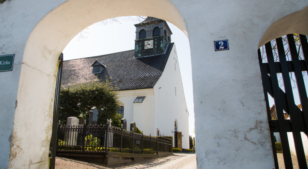 Kik gennem en port i en kirkegårdsmur mod en kirke