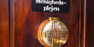 En gammeldags kirkebøsse hænger på en kirkedør. Kirkebøssen samler ind til menighedsplejen, som tager sig af sognets udsatte og fattige