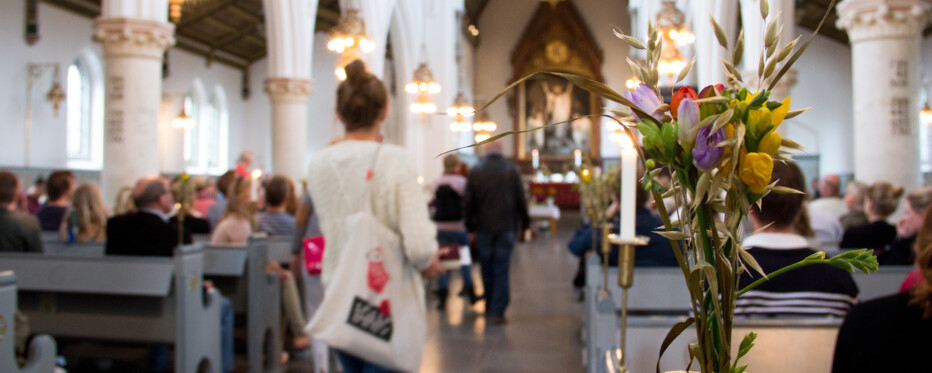 Mennesker på vej op ad kirkegulv i en fyldt kirke. En buket blomster i forgrunden