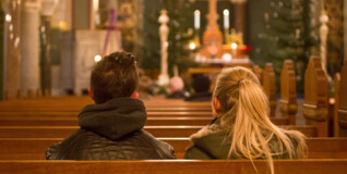 to unge mennesker sidder på en kirkebænk i en kirke iklædt overtøj. Kirken er tom, men det er jul