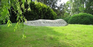 På en høj af grønt græs ligger en aflang sten på toppen med navnet "knud rasmussen" hugget foran.