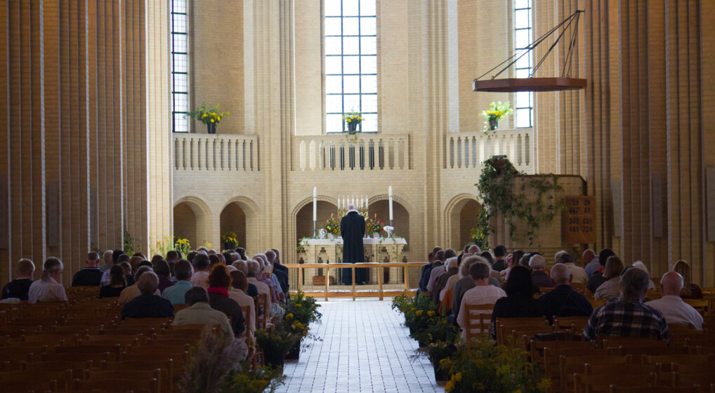 Kirkerum med en præst ved alteret og en siddende menighed