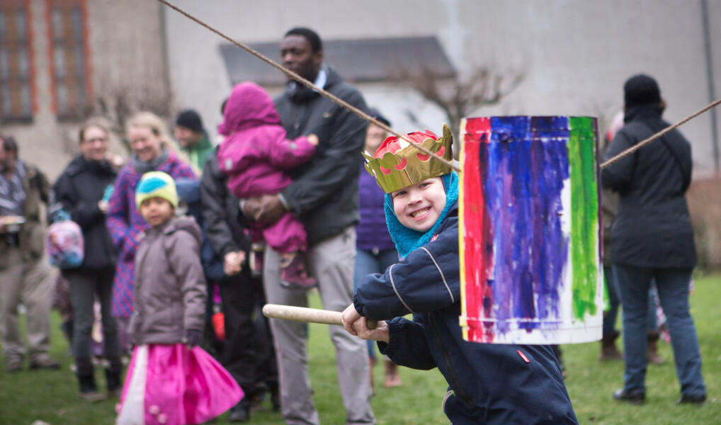 En dreng med kongekrone lægger an til et slag på fastelavnstønden