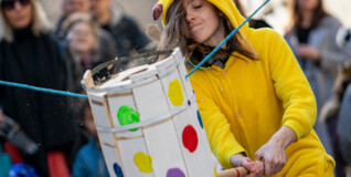 A kid dressed in a yellow Pikachu costume swings a club at a decorated barrel