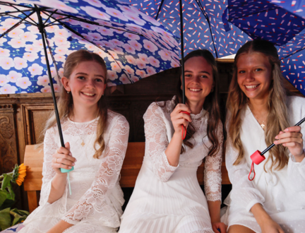 Tre konfirmander sidder på en kirkebænk med hver deres lille paraply