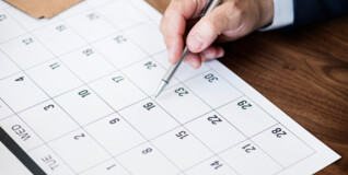 En hånd med en kuglepen er ved at notere noget i en kalender på et bord