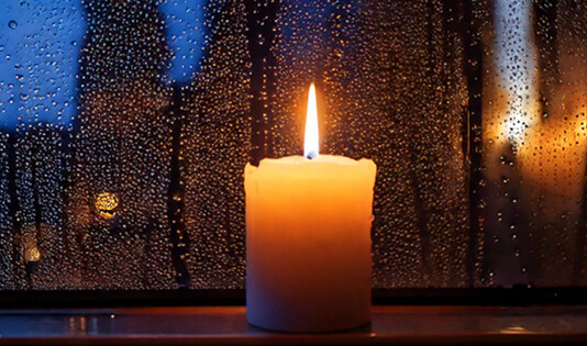 Et steatinlys brænder roligt i en vindueskarm bag en regnvåd rude