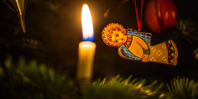 Et lys på et juletræ brænder stille foran en engel, der hænger fra en gren