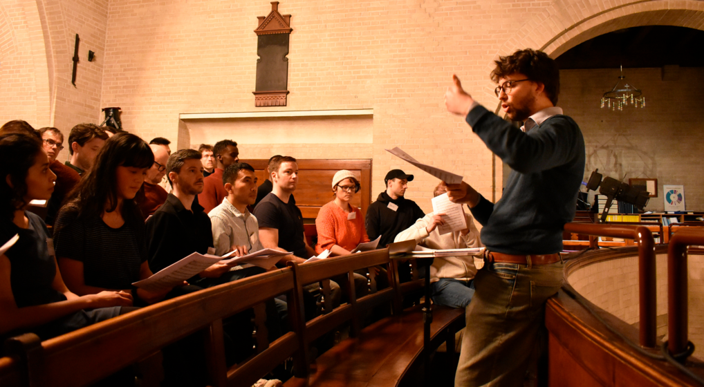 New International Choir - rehearsal A choir rehearsing in a church. The conductor waves his hands as he gives out instructions.