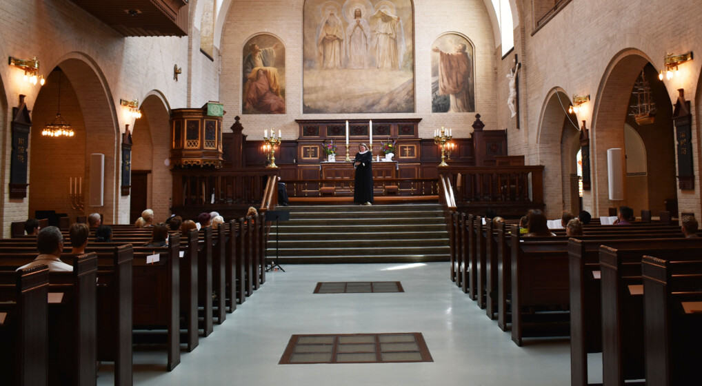 Inside the Elias Church during a Sunday Jazz Service. In front of the altar, Pastor Maria reads aloud from the Bible whilst church goers listen attentively