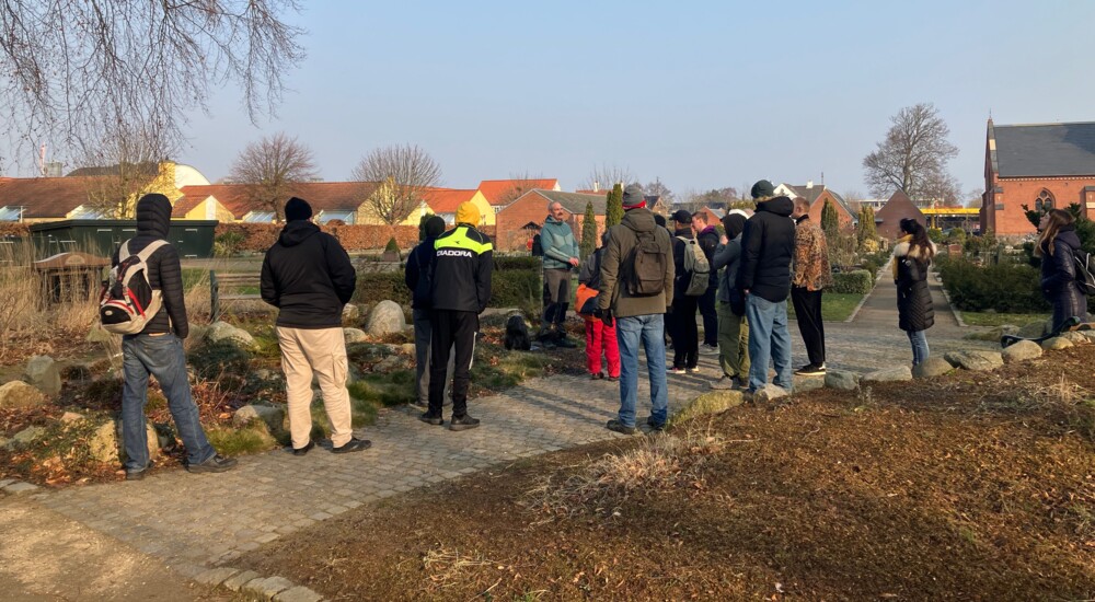 Elever fra anlægsgartneruddannelsen lytter mens en kirkegårdsansvarlig fortæller