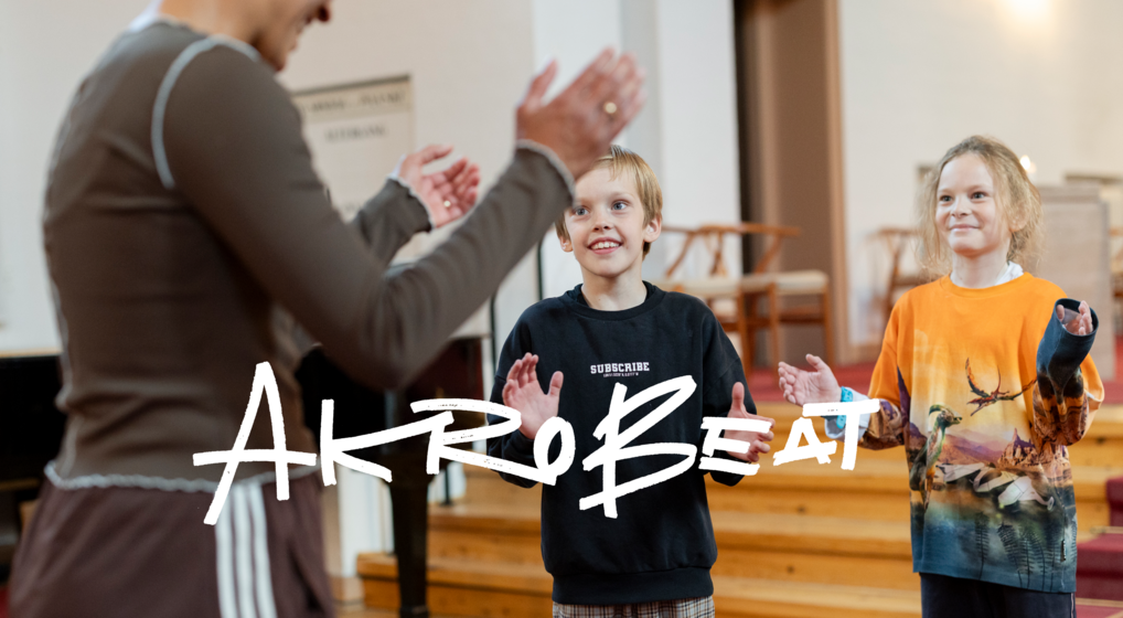 To drenge indenfor i Aalholm Kirke står foran akrobeat-instruktøren som viser en koreografi. Drengene og instruktøren er ved at klappe i hænderne.