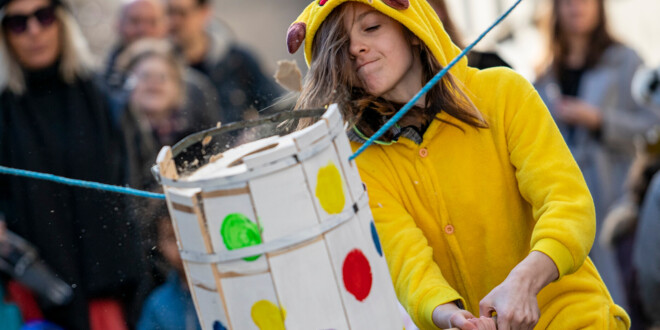 A kid dressed in a yellow Pikachu costume swings a club at a decorated barrel