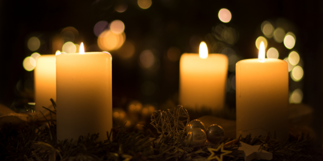 En adventskrans med alle fire lys tændt står stille i mørket